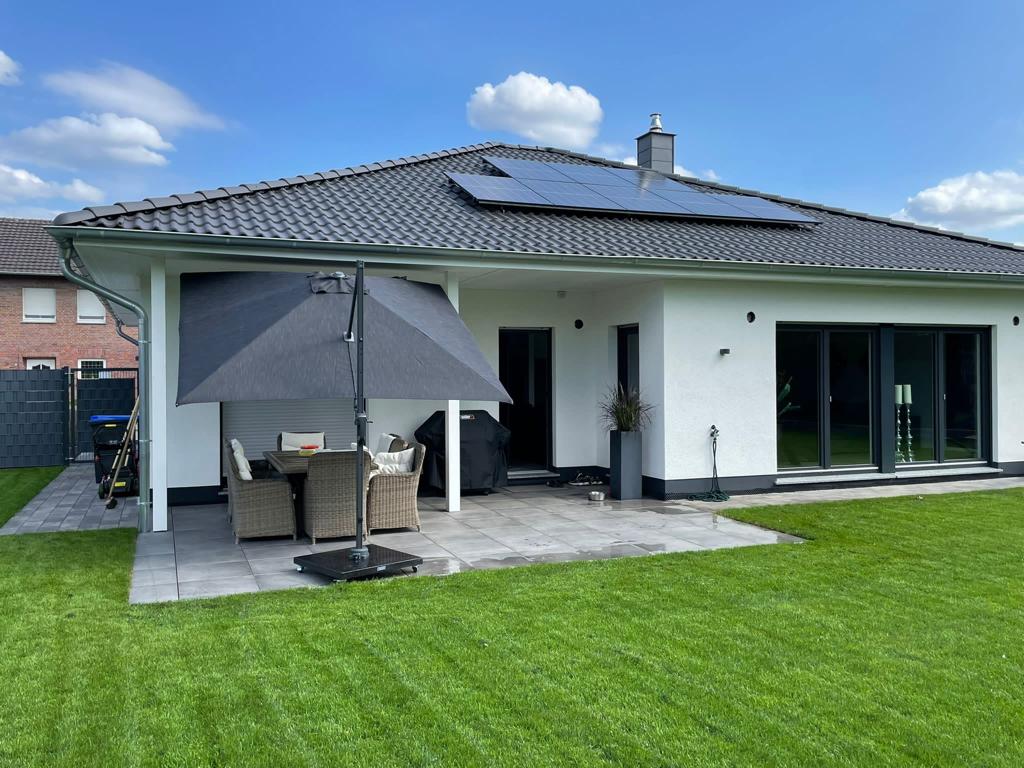Moderner Bungalow mit Terrasse, Markise und gepflegtem Rasen im Garten.